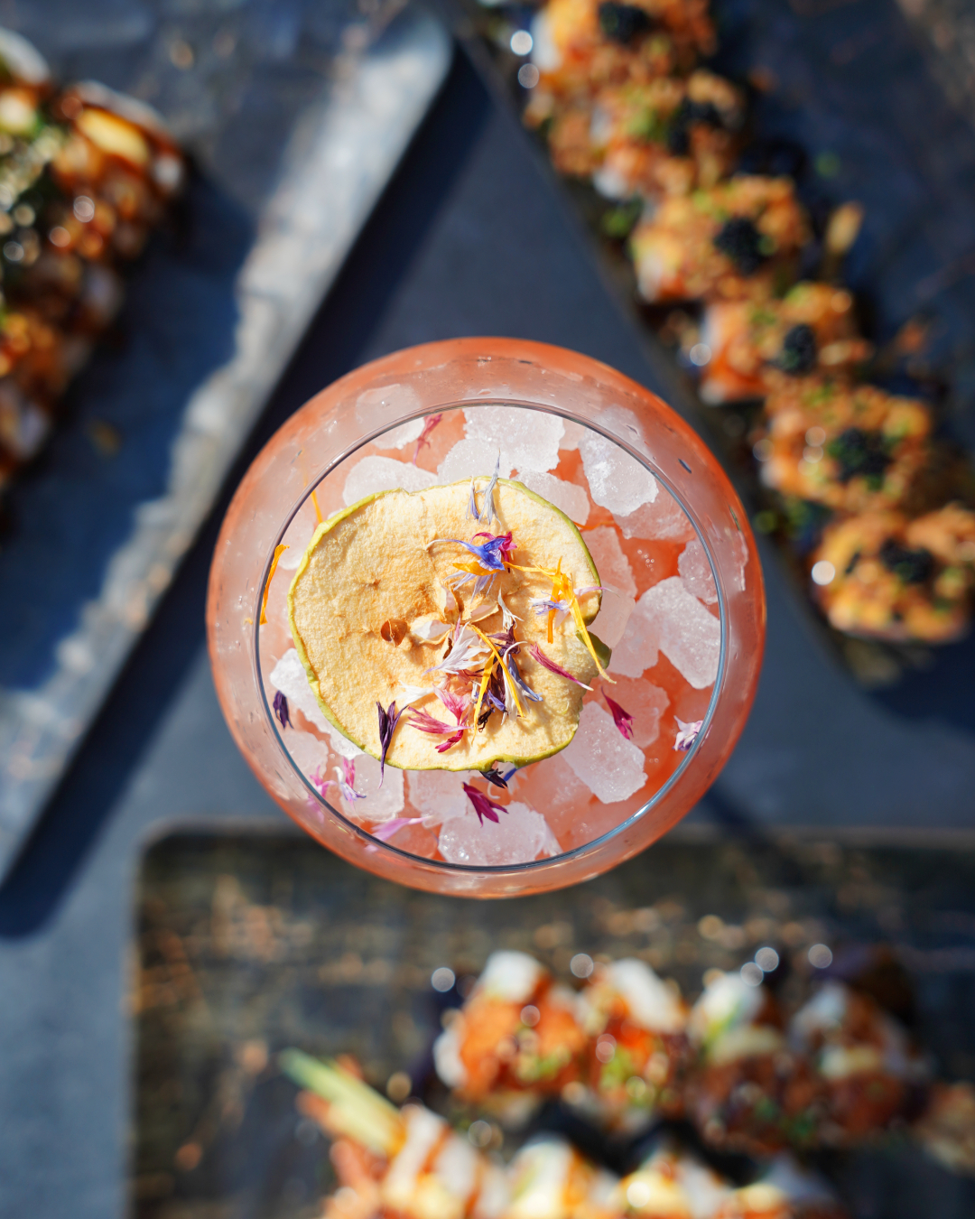 Overhead view of a cocktail garnished with dried apple and flowers